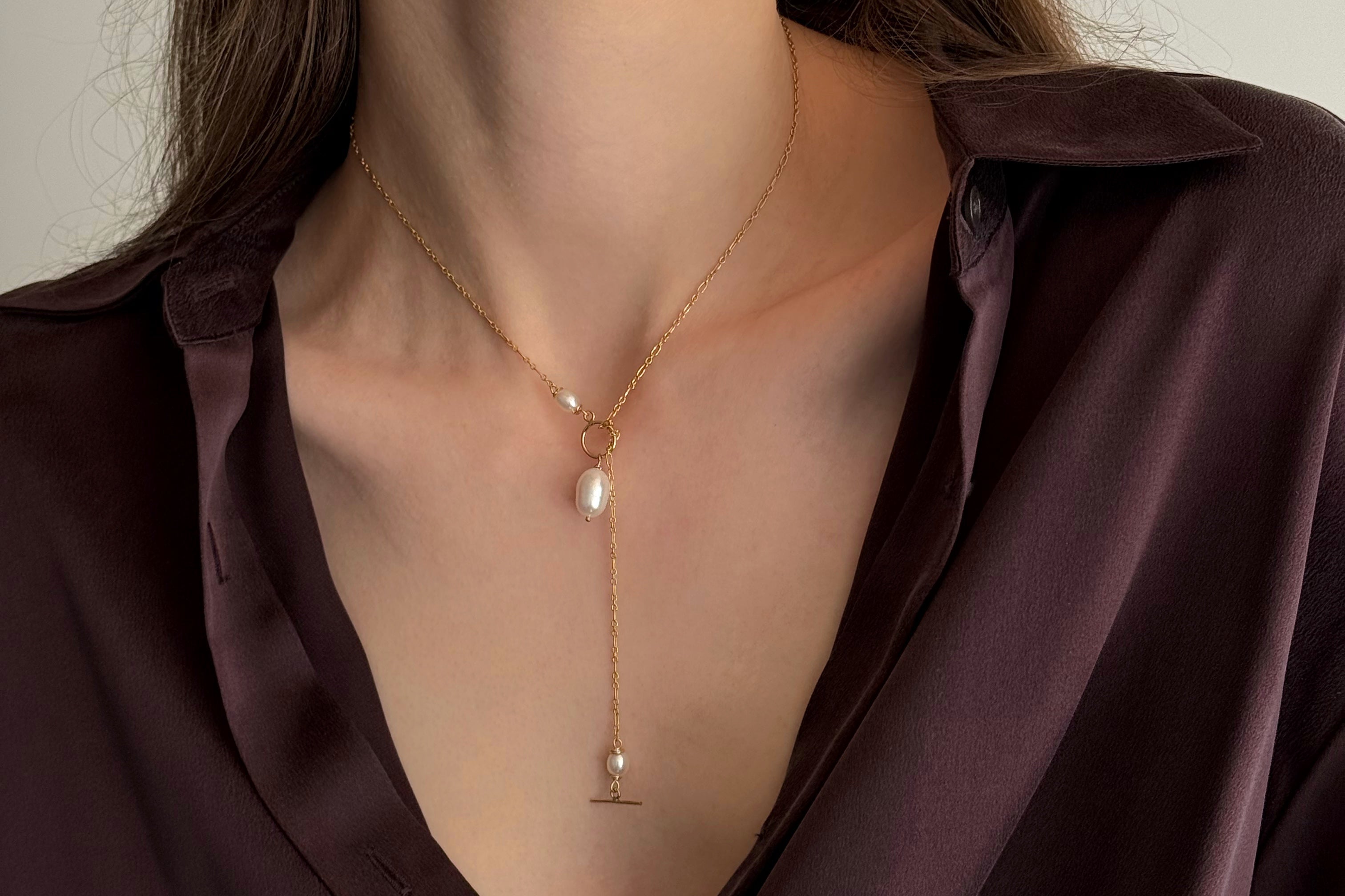 Close-up of a person wearing a delicate gold necklace with a pearl pendant.