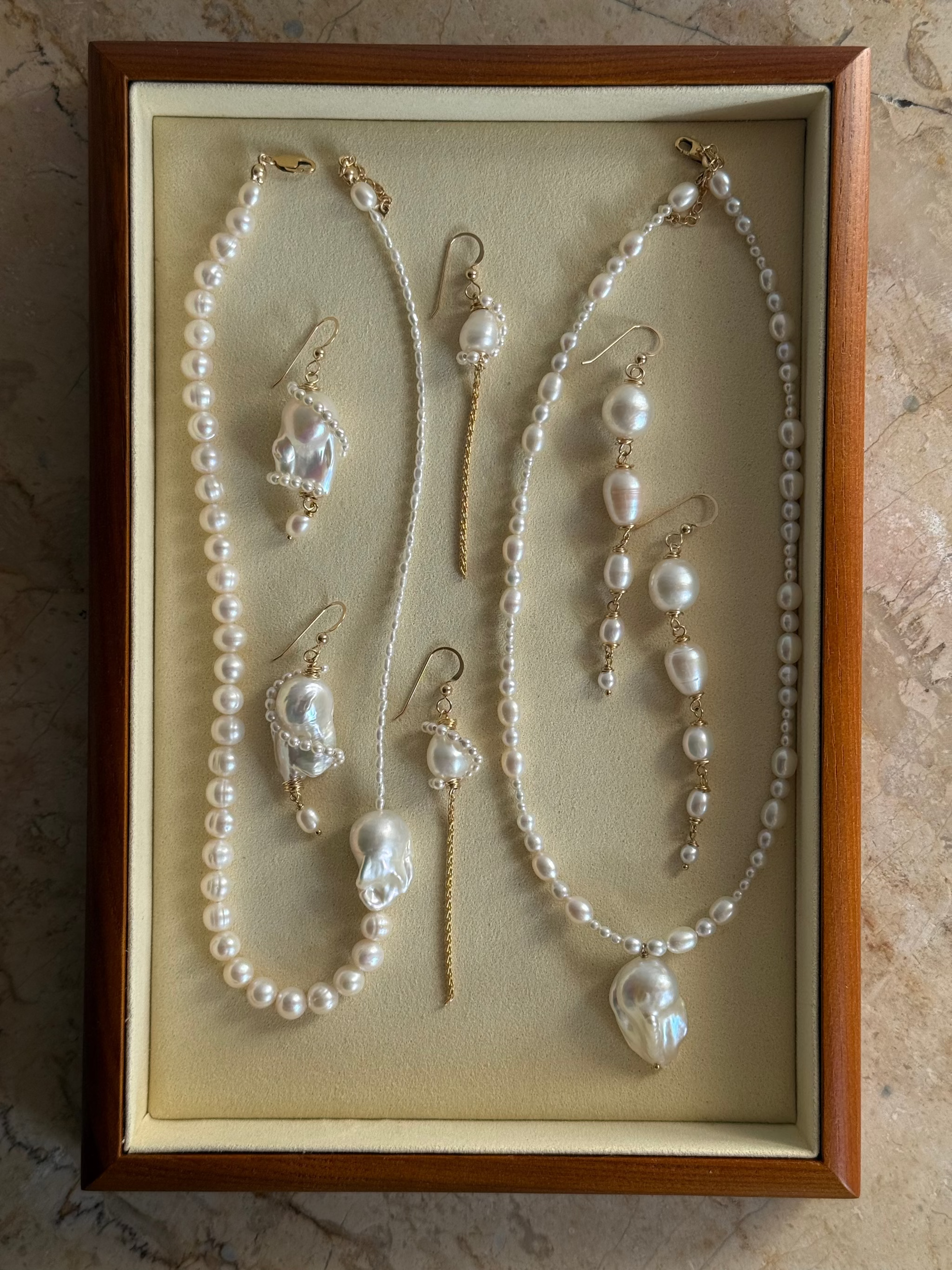 A jewelry set displayed inside a wooden presentation box with a beige interior. The set includes pearl necklaces, matching drop earrings, and a small pearl pendant on 14k gold filled chains.