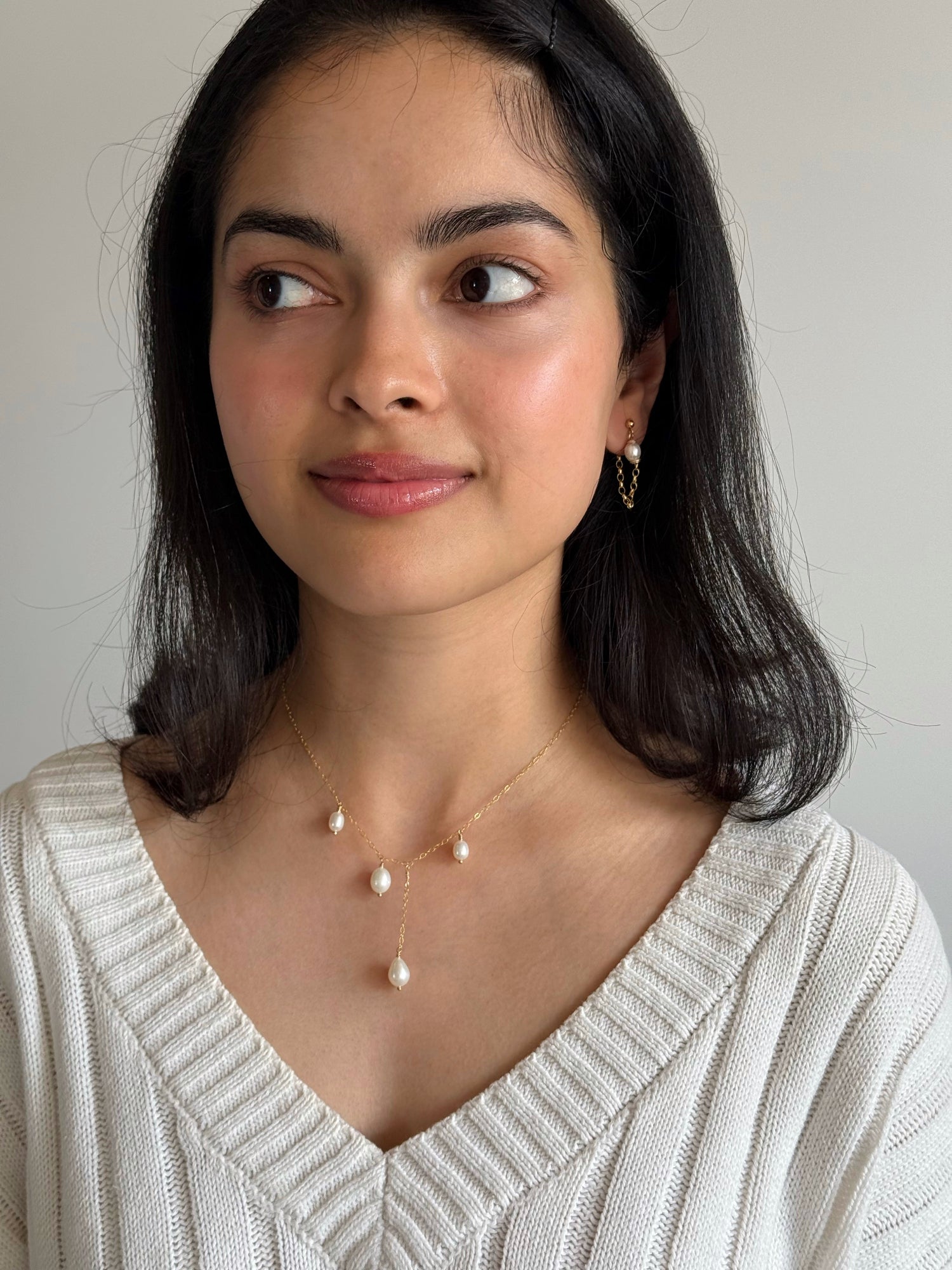 Woman wearing a pearl necklace and earrings against a neutral background