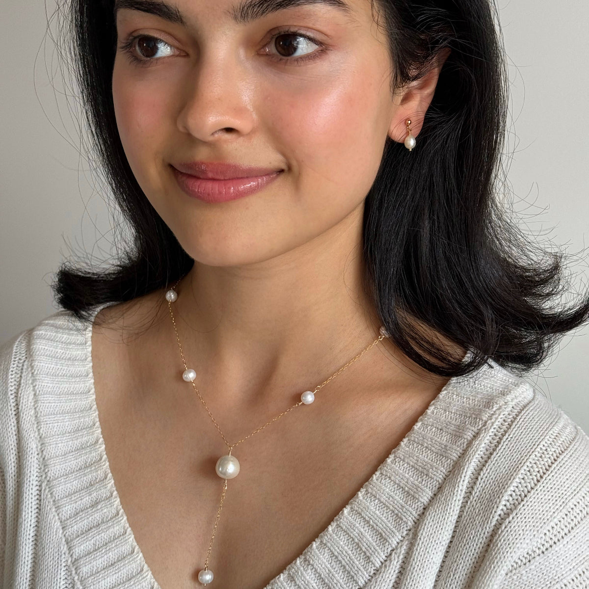 Woman wearing a gold-filled pearl necklace and pearl earrings against a neutral background