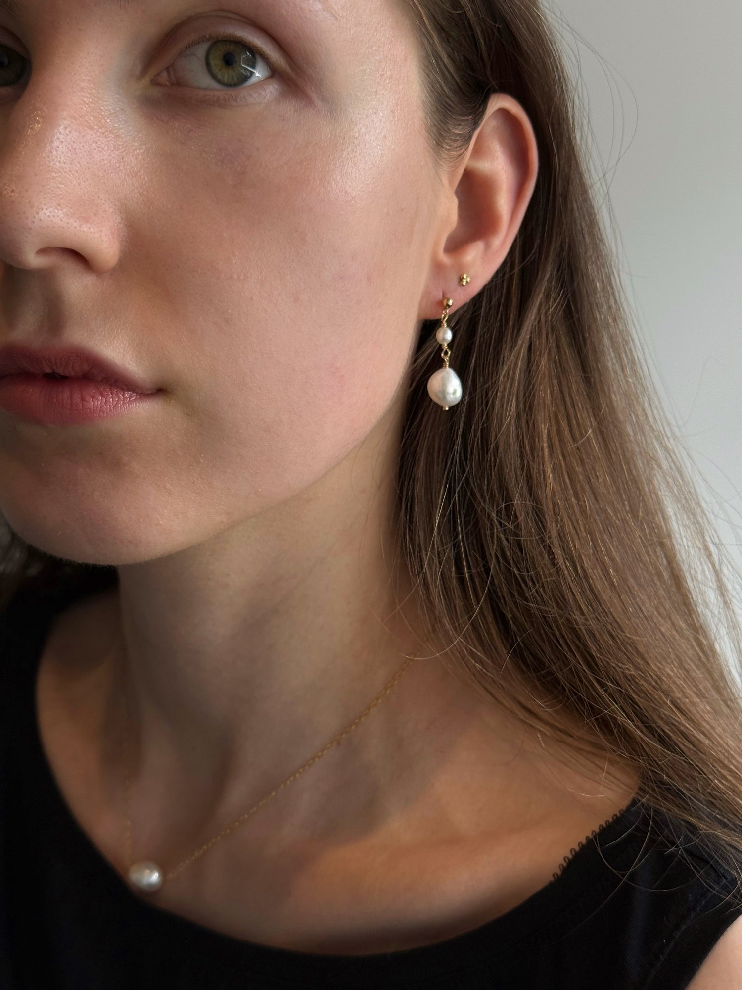 Close-up of a woman wearing pearl earrings with a neutral background