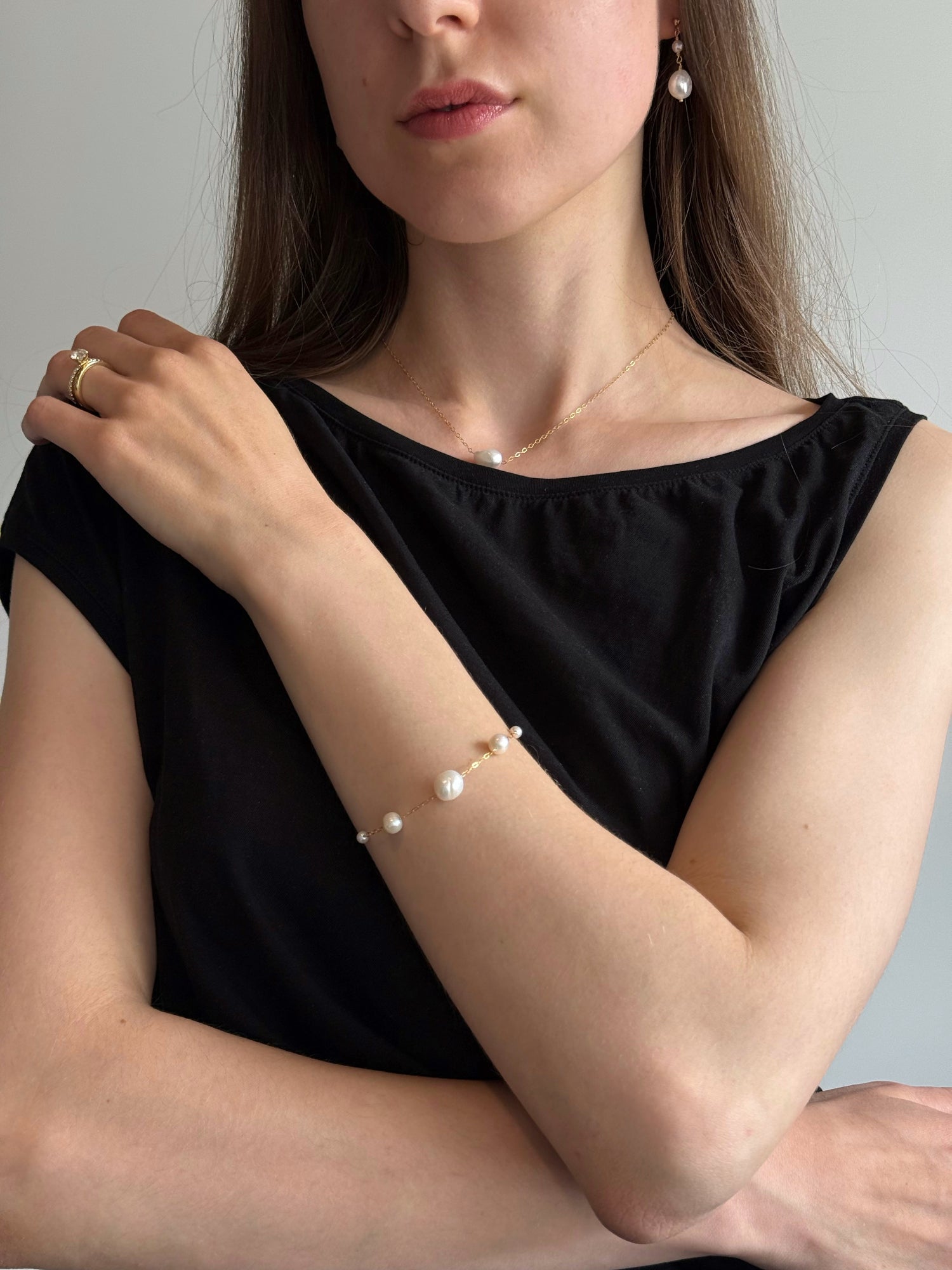 Woman wearing a black top with a pearl bracelet and earrings against a neutral background