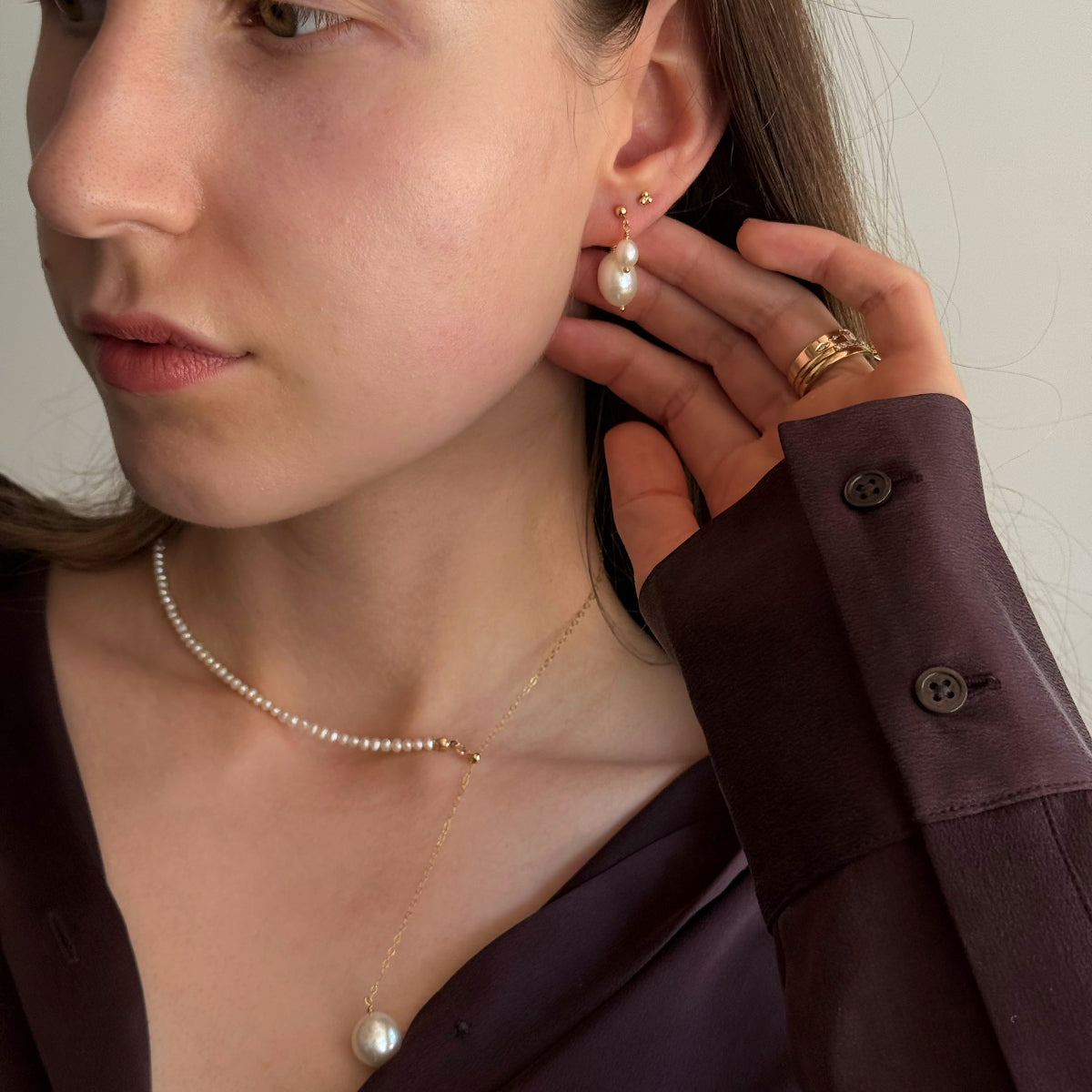 Woman wearing pearl earrings and a necklace, adjusting her earring.